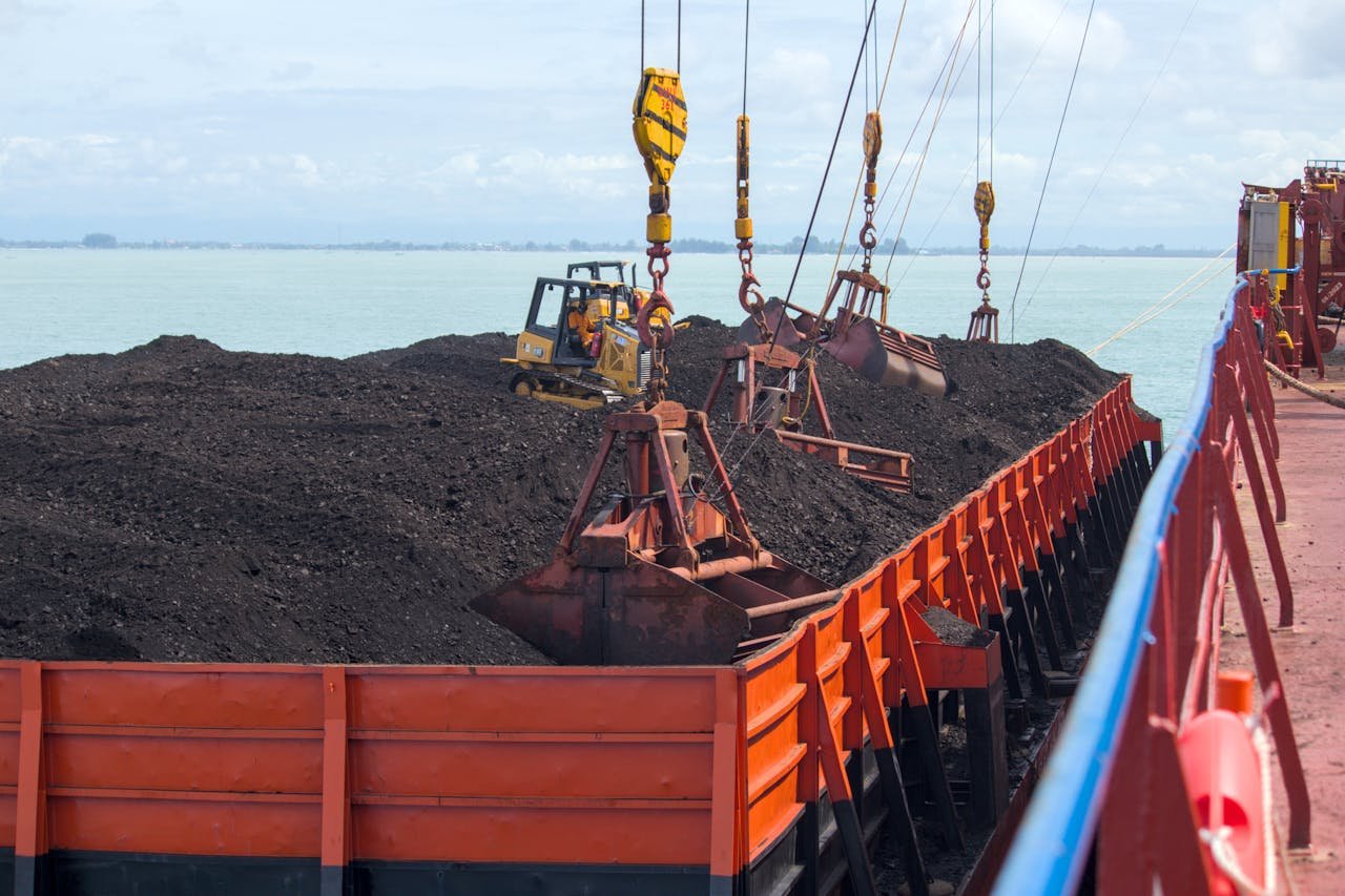hero-img-02 Heavy machinery loading coal onto a cargo ship at a seaport with cranes.